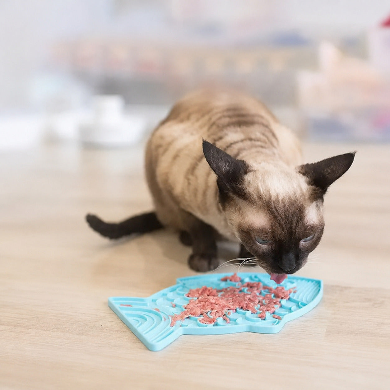 Cat using a Blue fish-shaped slow feeder lick mat with wet food